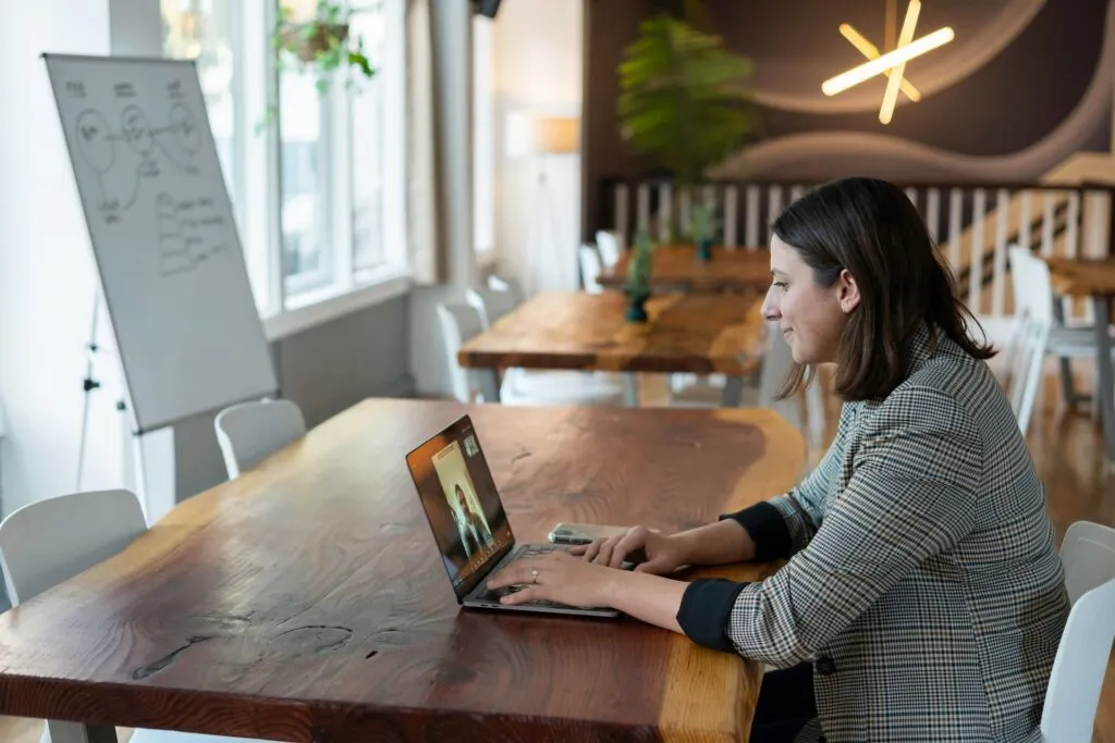 Smiling woman on a video call from an empty meeting room, using a laptop
